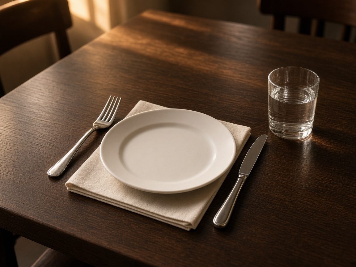 A place setting on a dining table, with a plate, napkin, and water glass. No people.